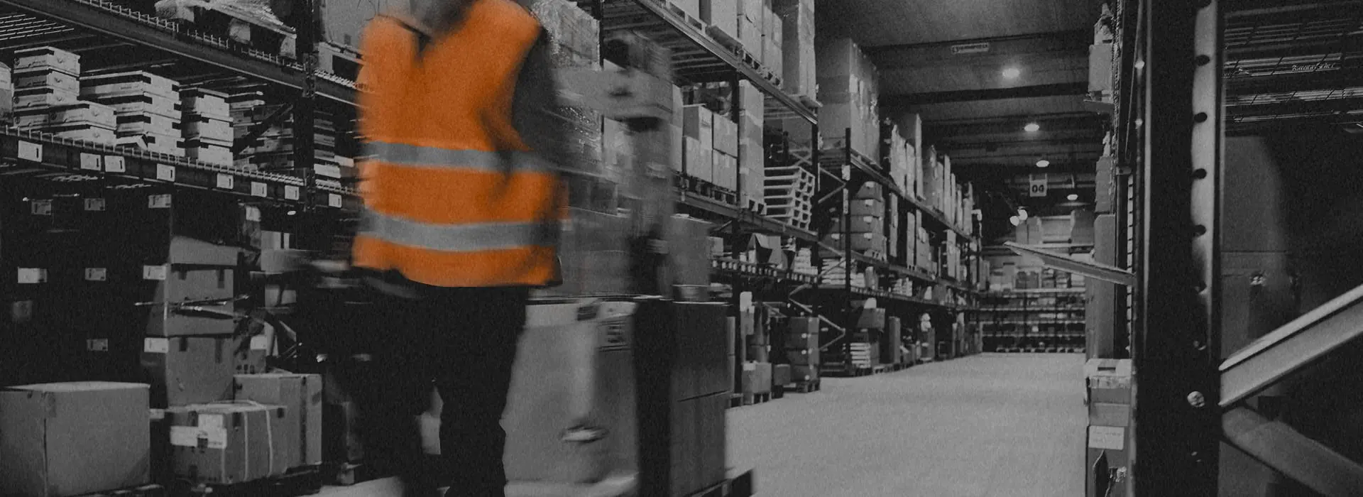A low-color photograph of a person in protective gear moving items through a warehouse