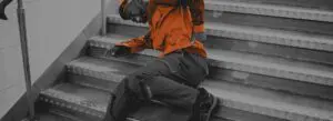 A low-color photograph of a person holding their lower back in pain on a staircase